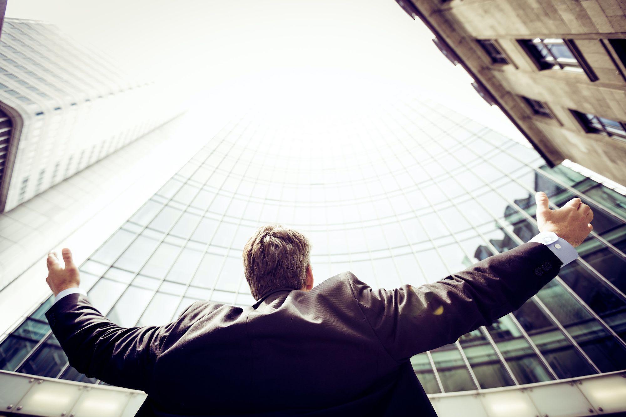 person in a suit with arms wide open looking up at a glass building