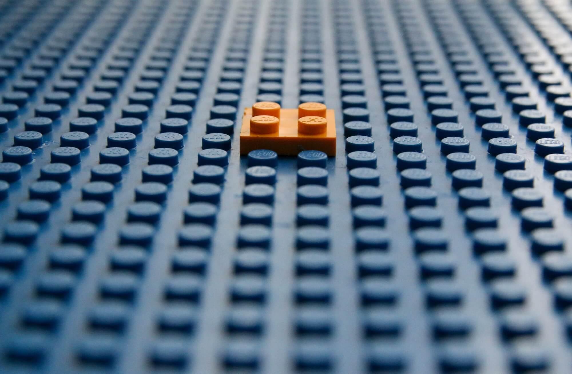 blue lego board with one square orange piece of lego attached in the centre of it
