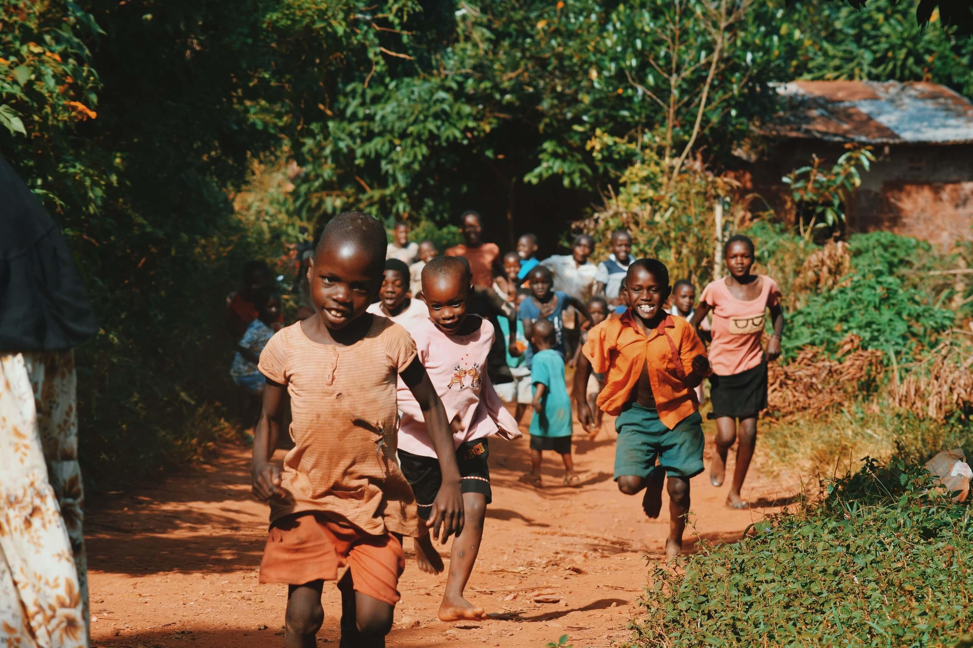Group of children in a village running barefoot towards the camera smiling and laughing.