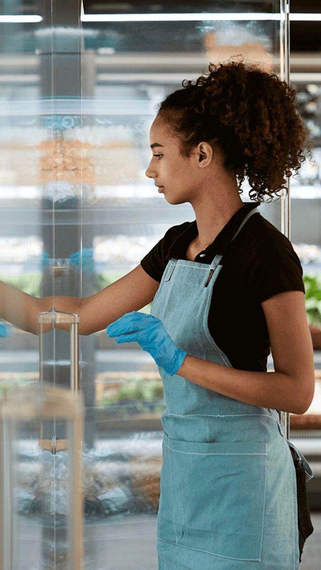 Woman with gloves and an apron on putting items into a refrigeration unit.