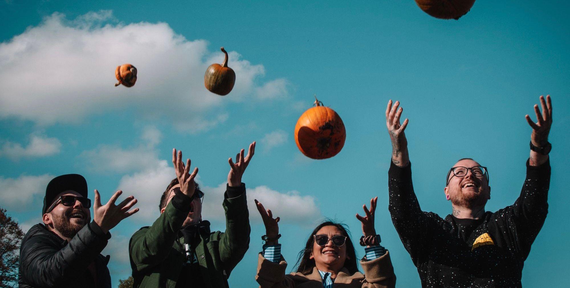 Four people throwing pumpkins in the air and smiling.